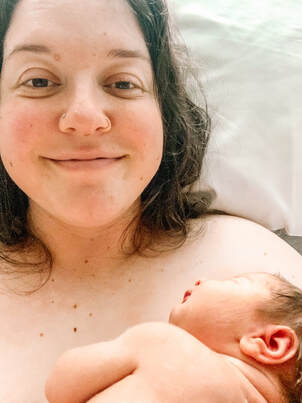A new parent smiling and looking directly at the camera while holding her brand new baby.