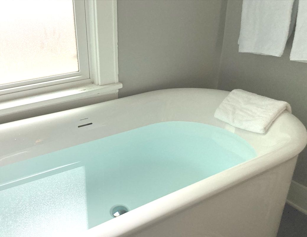 Large white bathtub filled with warm water, with a bath pillow on one end.